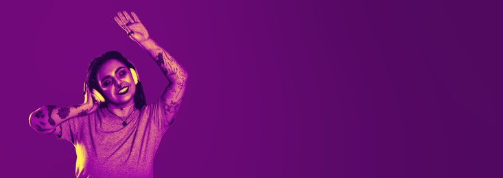 Image of Beautiful young woman with tattoos on arms, nose piercing and dreadlocks listening to music in neon light, space for text. Banner design