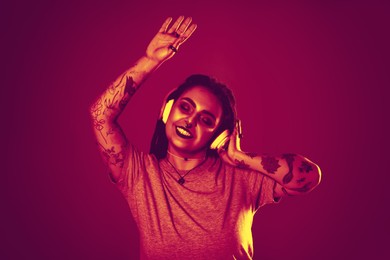 Image of Beautiful young woman with tattoos on arms, nose piercing and dreadlocks listening to music in neon light