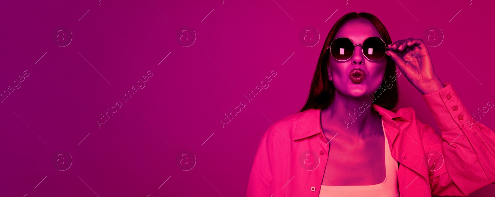 Image of Attractive happy woman with fashionable sunglasses in neon light, space for text. Banner design