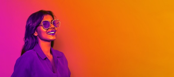 Image of Happy beautiful woman with stylish sunglasses in neon light, space for text. Banner design