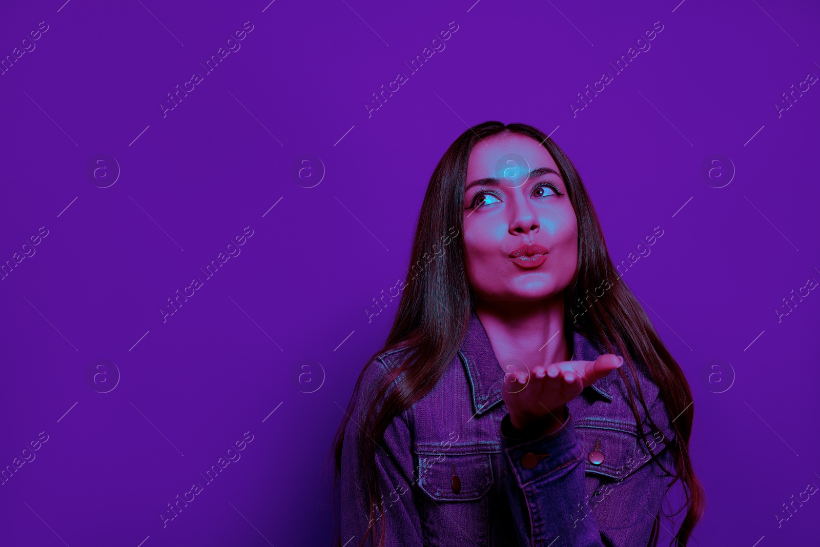 Image of Beautiful young woman blowing kiss in neon light, space for text