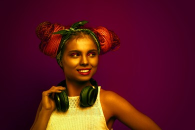 Image of Beautiful woman with braided double buns and headphones in neon light, space for text