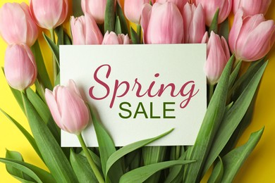 Image of Spring Sale card and pink tulips on yellow background, top view. Seasonal discount