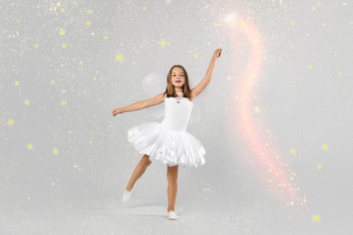 Image of Cute girl with fairy wings conducting spell on grey background. Magic lights around