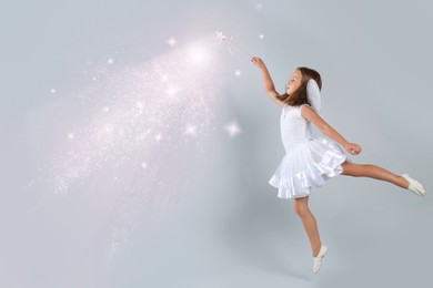 Image of Cute girl with fairy wings conducting spell on grey background. Lights coming from magic wand