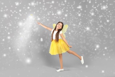 Image of Cute girl with fairy wings conducting spell on grey background. Magic lights around