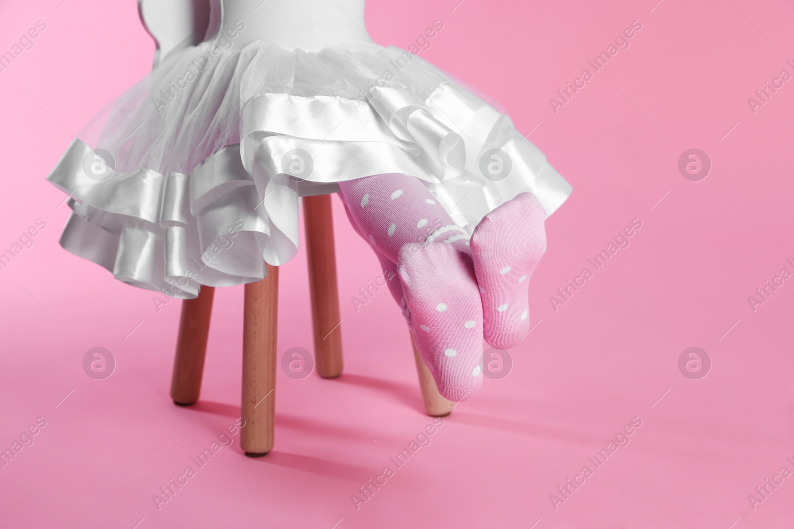 Photo of Child in tights sitting on stool against pink background, closeup. Space for text