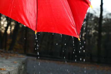 Photo of Open red umbrella under pouring rain outdoors, closeup