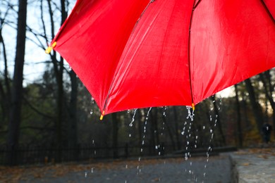 Photo of Open red umbrella under pouring rain outdoors, closeup