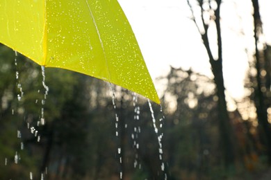 Photo of Open yellow umbrella under pouring rain outdoors, closeup