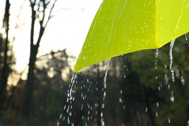 Photo of Open yellow umbrella under pouring rain outdoors, closeup