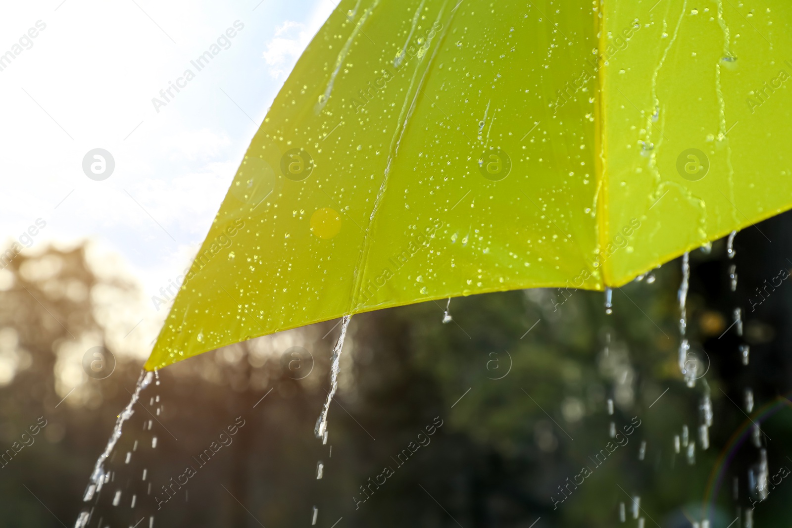 Photo of Open yellow umbrella under pouring rain outdoors, closeup