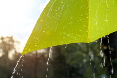 Photo of Open yellow umbrella under pouring rain outdoors, closeup