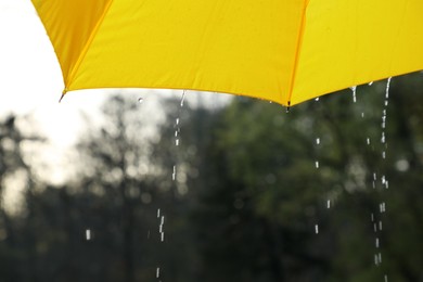 Photo of Open yellow umbrella under pouring rain outdoors, closeup