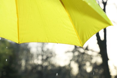 Photo of Open yellow umbrella under pouring rain outdoors, closeup