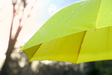 Photo of Open yellow umbrella under pouring rain outdoors, closeup