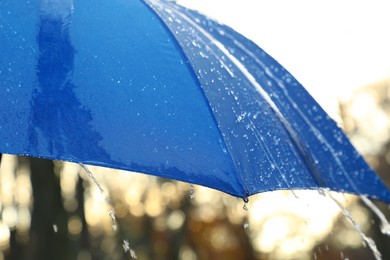 Photo of Open blue umbrella under pouring rain outdoors, closeup