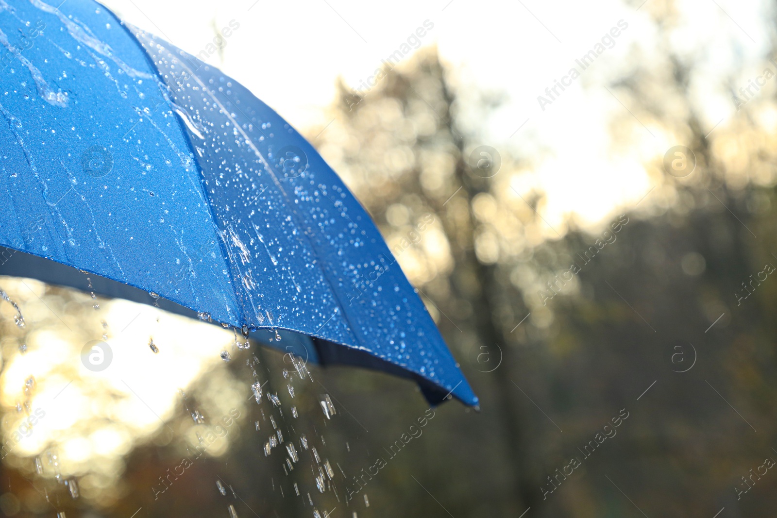 Photo of Open blue umbrella under pouring rain outdoors, closeup. Space for text