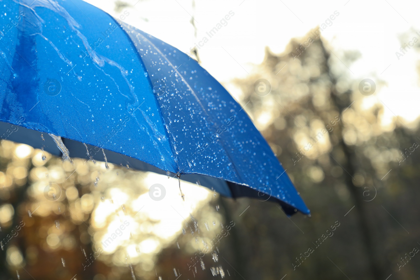 Photo of Open blue umbrella under pouring rain outdoors, closeup