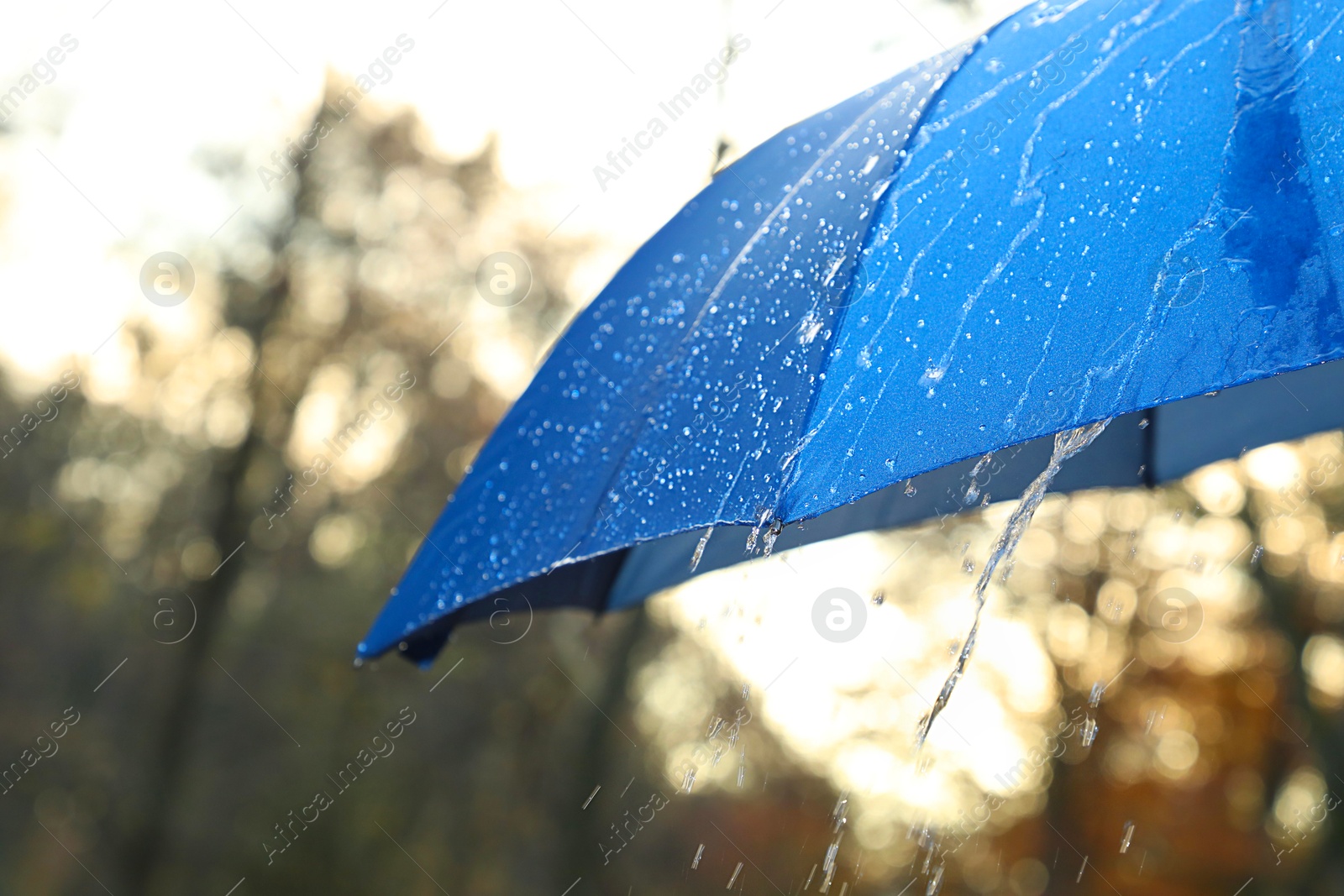 Photo of Open blue umbrella under pouring rain outdoors, closeup