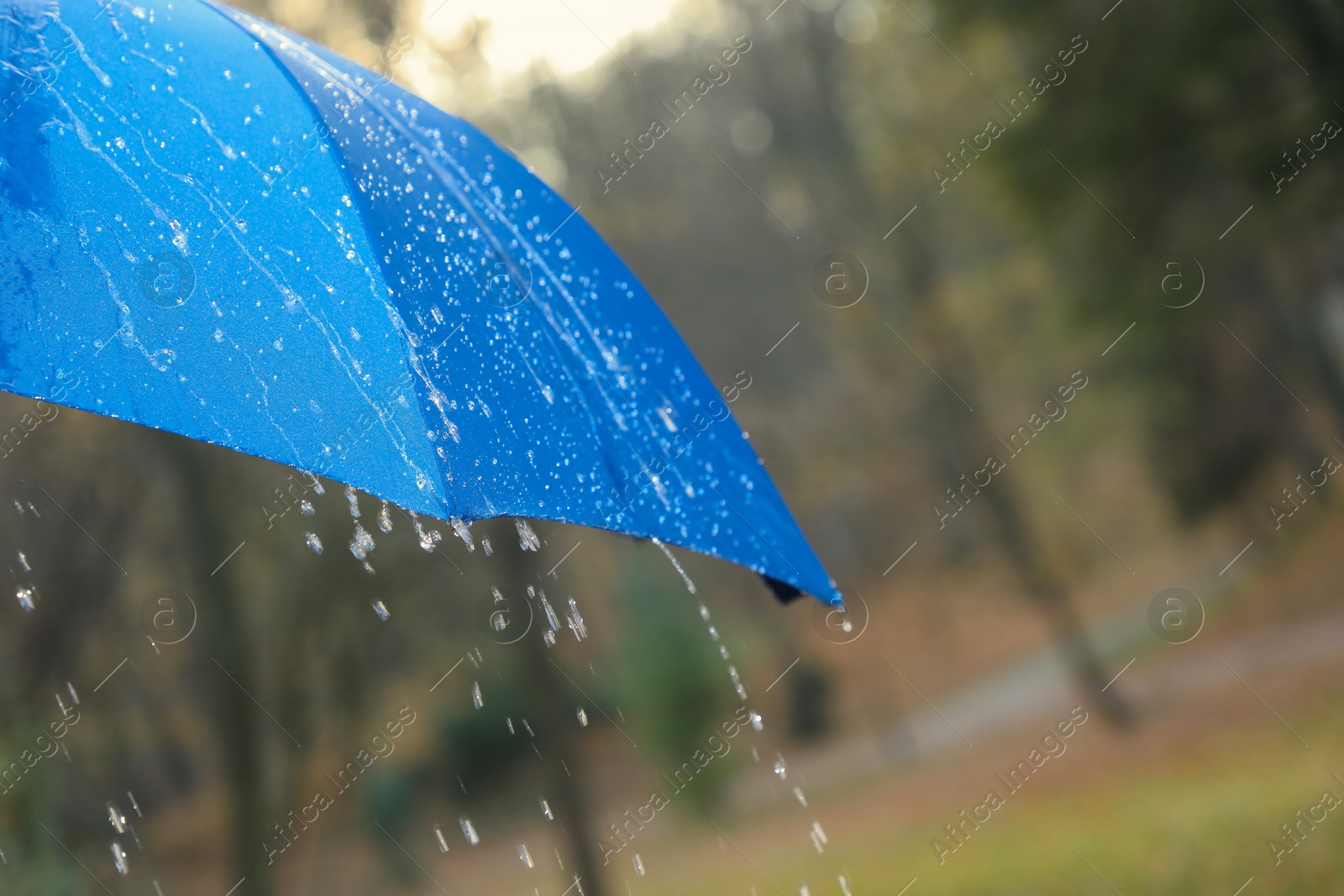 Photo of Open blue umbrella under pouring rain outdoors, closeup. Space for text