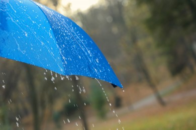 Photo of Open blue umbrella under pouring rain outdoors, closeup. Space for text