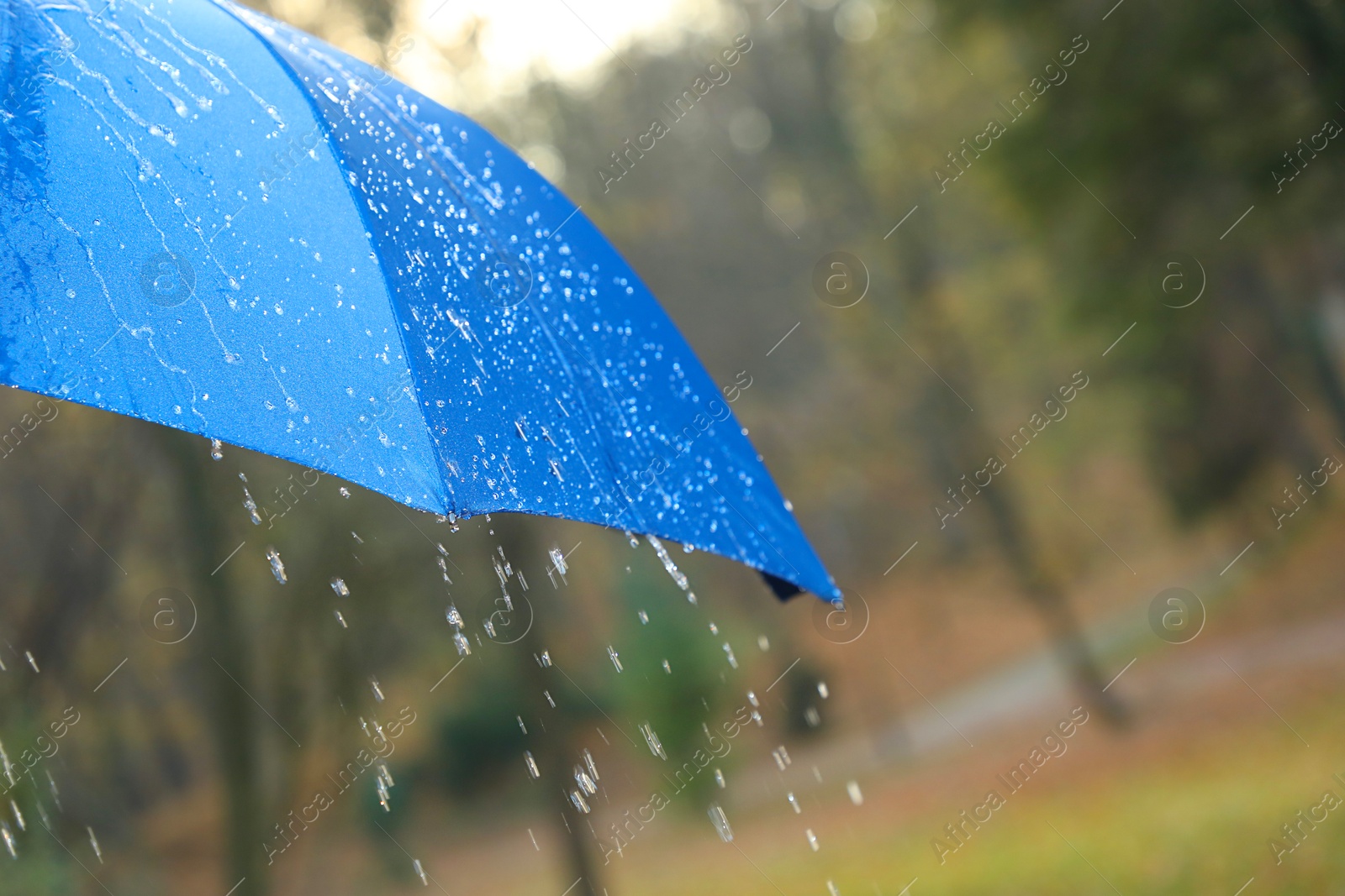 Photo of Open blue umbrella under pouring rain outdoors, closeup. Space for text