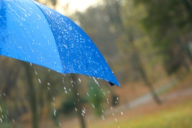 Photo of Open blue umbrella under pouring rain outdoors, closeup. Space for text