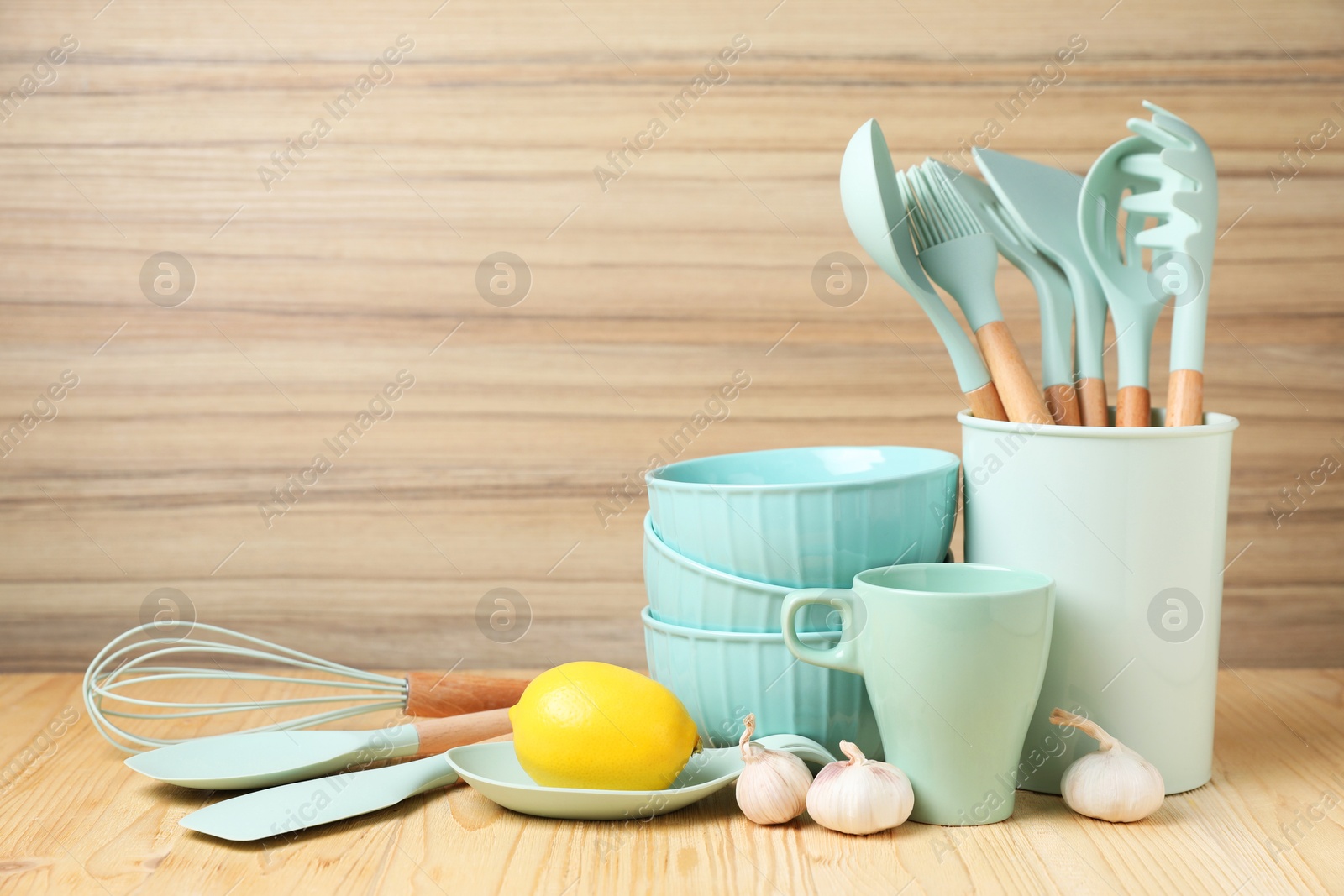 Photo of Dishware, cooking utensils, lemon and garlic on wooden table. Space for text