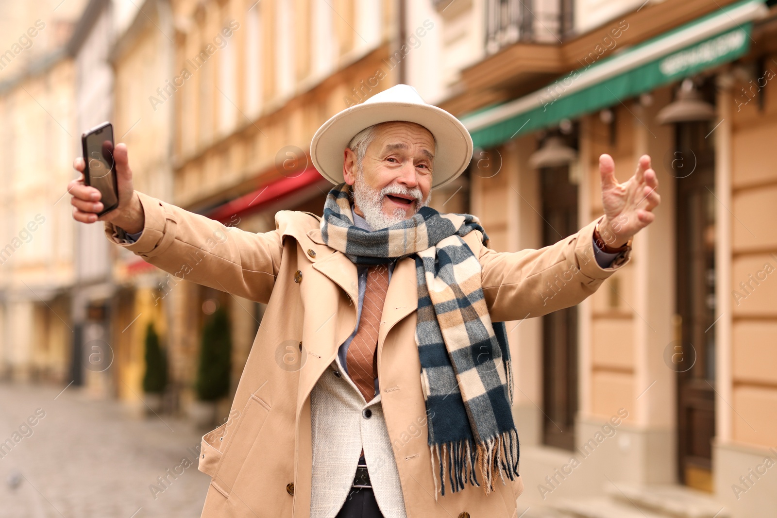 Photo of Emotional senior man with smartphone greeting someone on city street