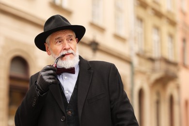 Photo of Stylish senior man with tobacco pipe on city street