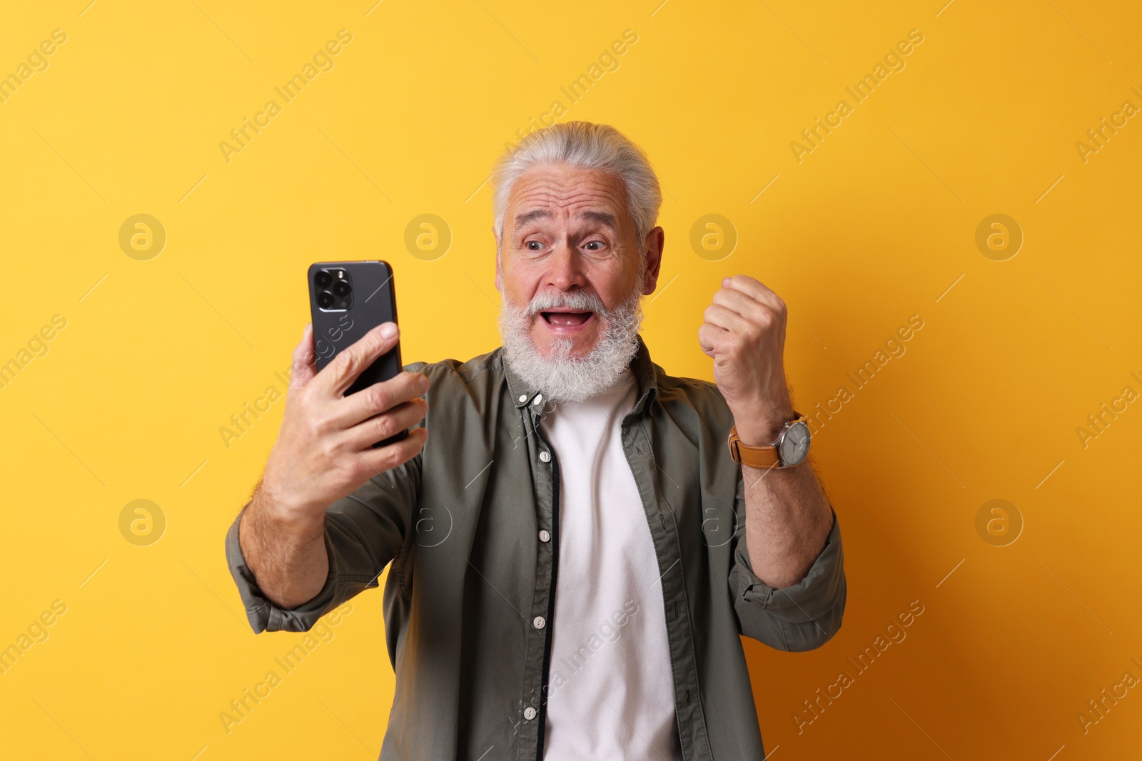 Photo of Emotional senior man with smartphone on orange background