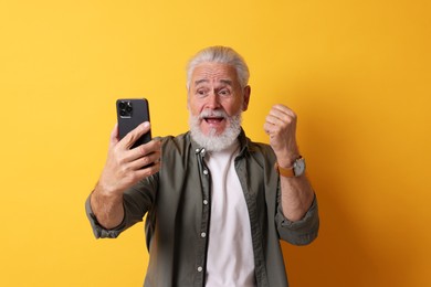 Photo of Emotional senior man with smartphone on orange background