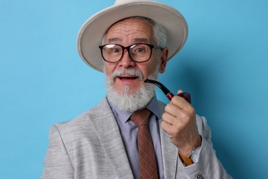 Photo of Stylish senior man with tobacco pipe on light blue background