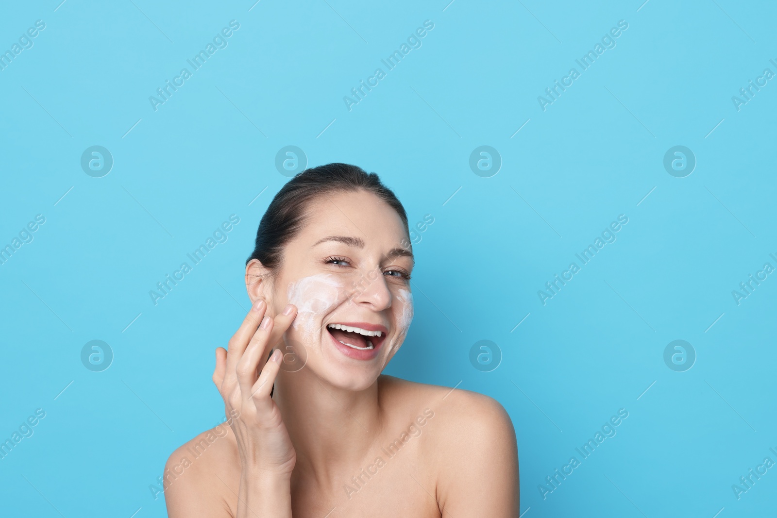 Photo of Spa day. Happy woman applying mask onto her face on light blue background