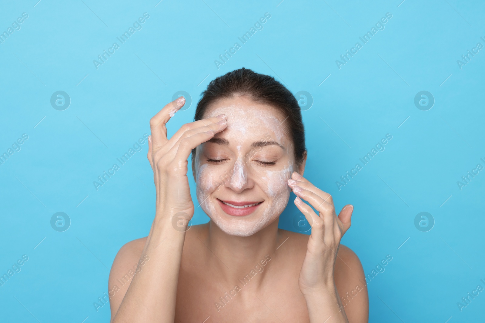 Photo of Spa day. Happy woman applying mask onto her face on light blue background