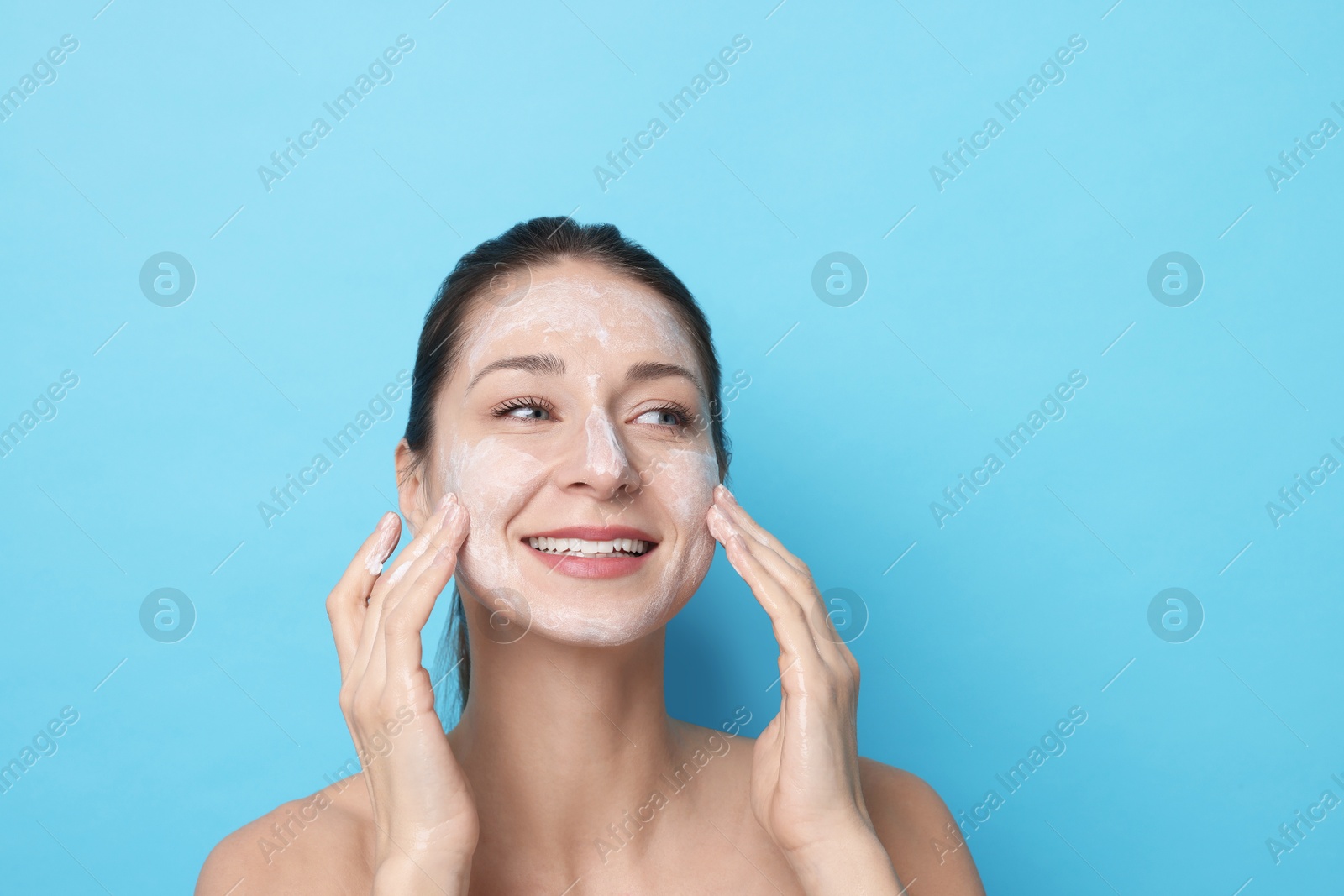 Photo of Spa day. Happy woman applying mask onto her face on light blue background