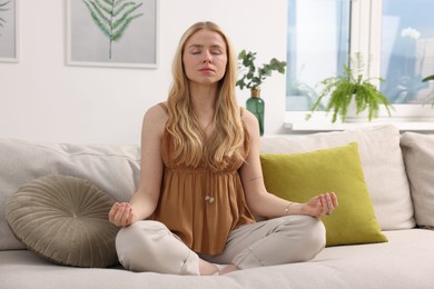 Photo of Feng shui. Young woman meditating on couch at home