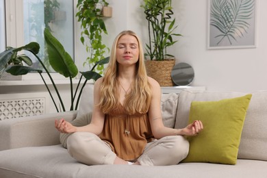 Photo of Feng shui. Young woman meditating on couch at home