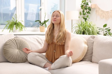 Photo of Feng shui. Young woman meditating on couch at home