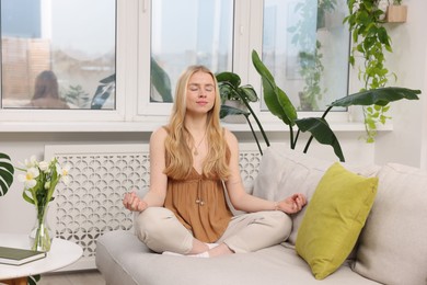 Photo of Feng shui. Young woman meditating on couch at home