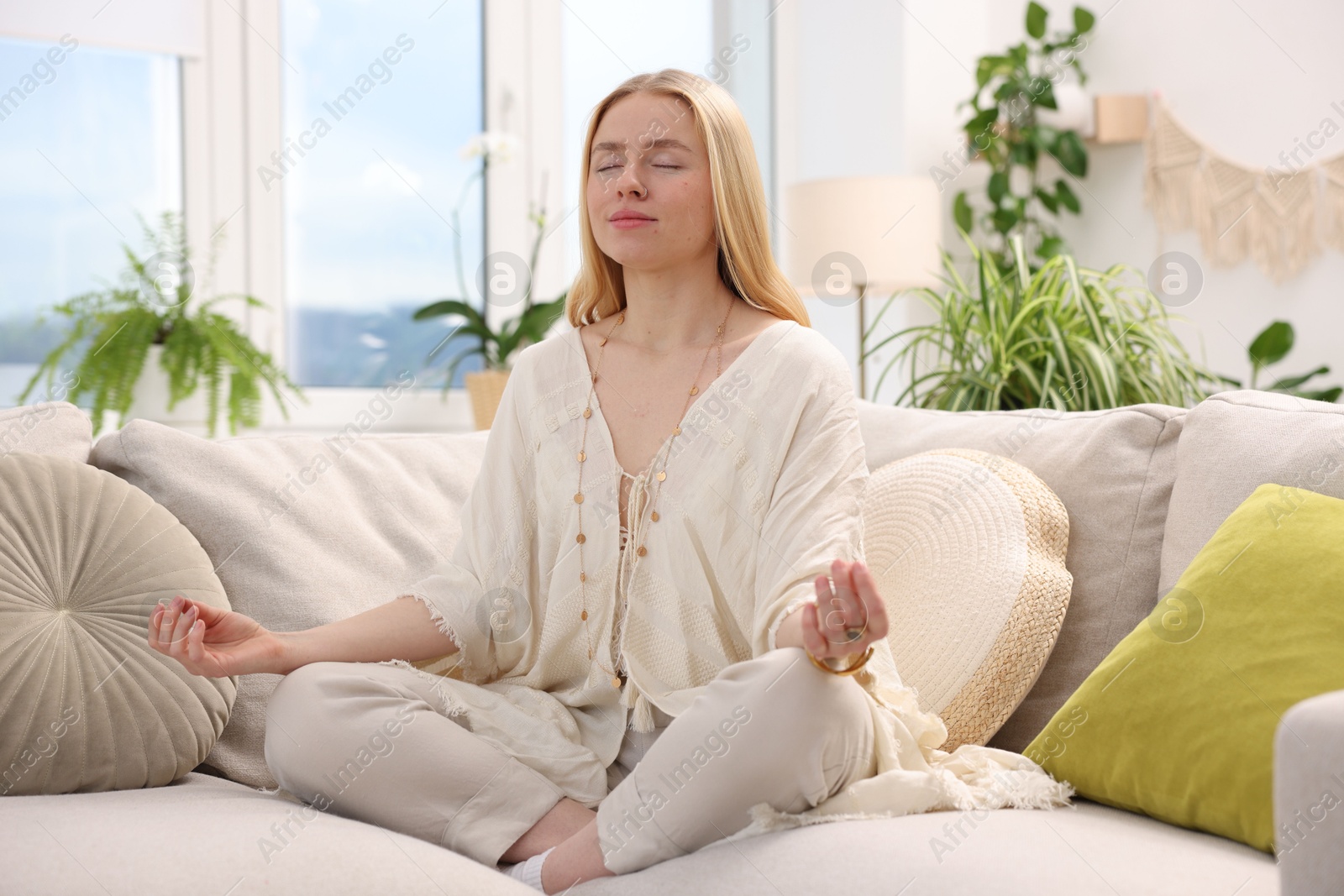 Photo of Feng shui. Young woman meditating on couch at home