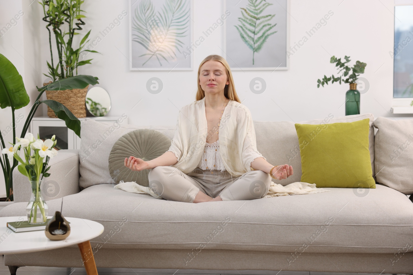 Photo of Feng shui. Young woman meditating on couch at home