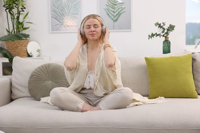 Photo of Feng shui. Young woman with headphones meditating on couch at home