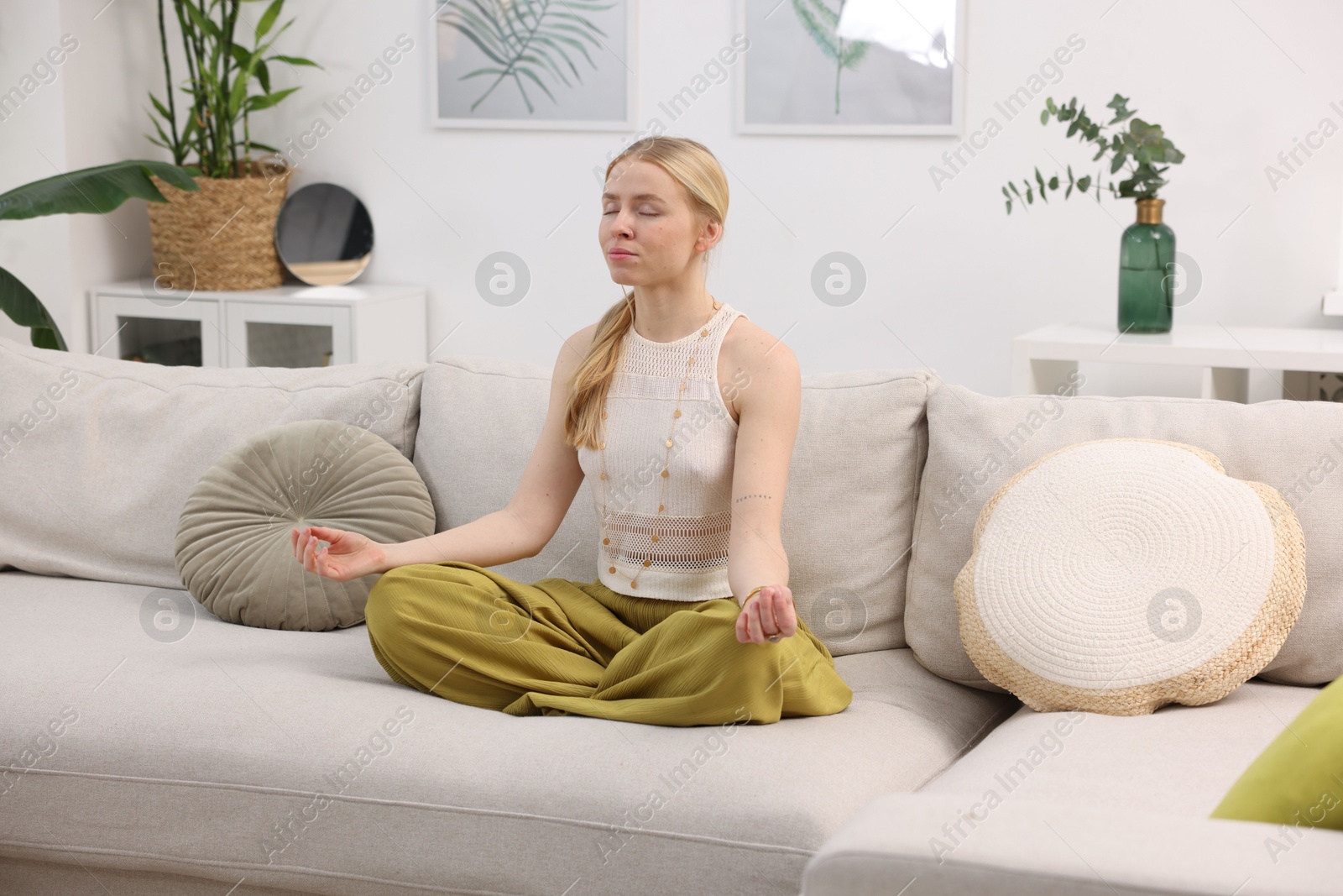 Photo of Feng shui. Young woman meditating on couch at home