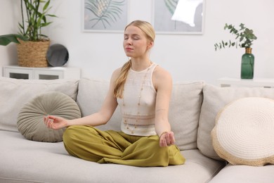 Photo of Feng shui. Young woman meditating on couch at home