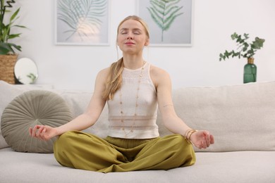 Photo of Feng shui. Young woman meditating on couch at home