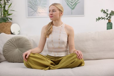 Photo of Feng shui. Young woman meditating on couch at home