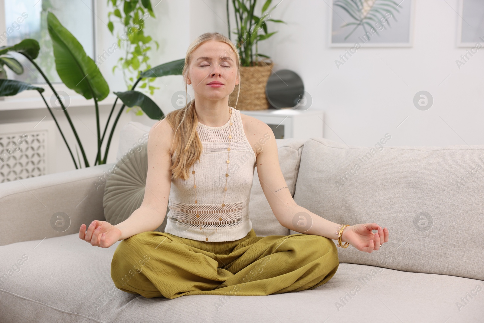 Photo of Feng shui. Young woman meditating on couch at home