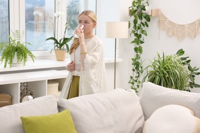 Photo of Feng shui. Young woman drinking water near houseplants at home